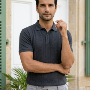 Homme portant un polo gris foncé texturé coupe classique avec un pantalon gris clair, posant devant une porte blanche.